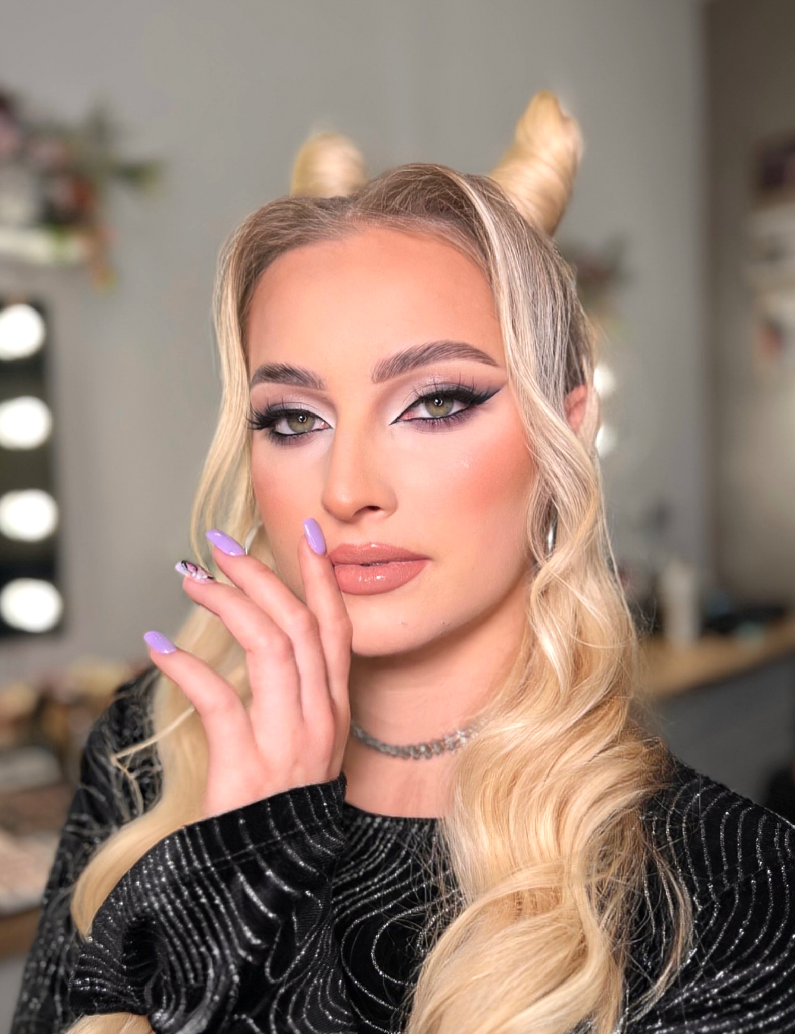 Portret kobiety z profesjonalnym makijażem oczu, błyszczącymi ustami i blond włosami upiętymi w nietypowe rogi, prezentującej fioletowy manicure.