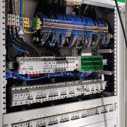 Energo Krzysztof Szpakowski - Rozdzielnica elektryczna PrismaSeT Schneider Electric z licznymi bezpiecznikami, przewodami i elementami łączeniowymi. Widok z bliska na wnętrze szafy sterowniczej.
