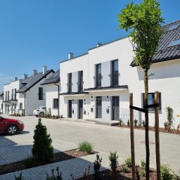 INVEST-DOM - Nowoczesne szeregowe domy z szarymi drzwiami wejściowymi, małymi balkonami i czarnymi oknami, widok z poziomu chodnika.