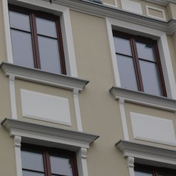 INVEST-DOM - Elewacja budynku z trzema oknami z brązowymi ramami i białymi dekoracyjnymi elementami architektonicznymi.