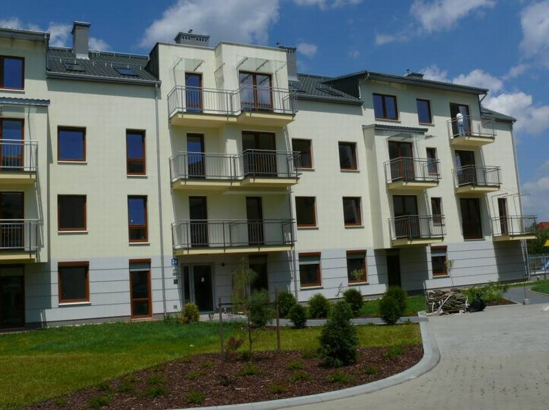 Nowoczesny apartamentowiec z balkonami i brązowymi ramami okiennymi, widok z poziomu chodnika w słoneczny dzień.