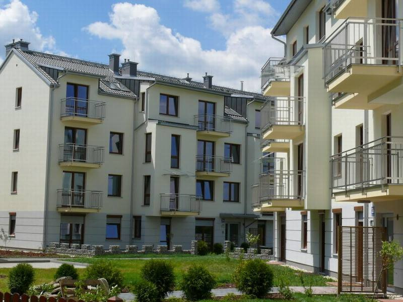 Nowoczesny budynek wielorodzinny z balkonami i oknami, widok z niskiej perspektywy na zadbany trawnik.