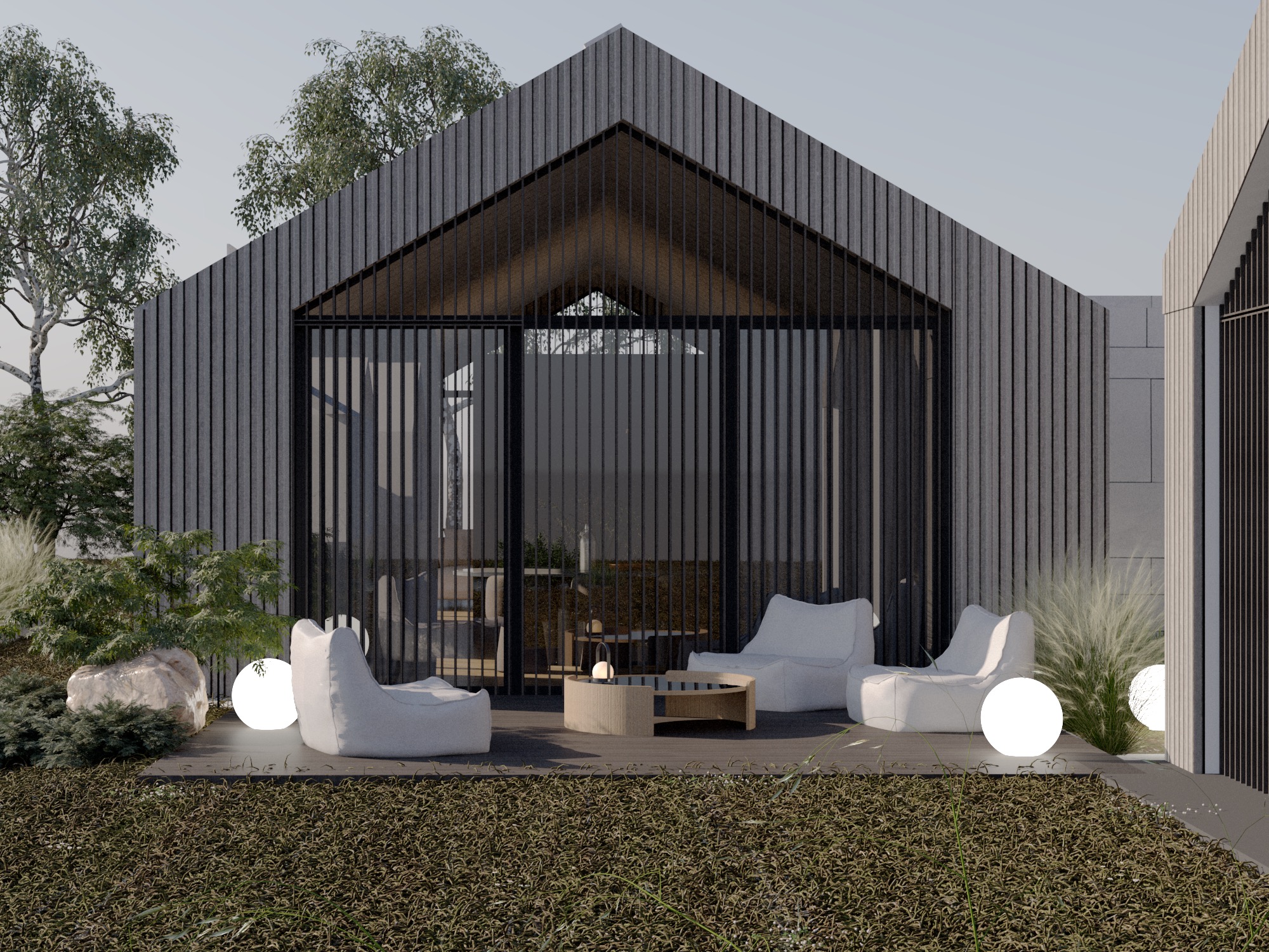 Nowoczesny taras z szarą elewacją domu, białymi pufami, okrągłym stolikiem kawowym i kulistymi lampami, otoczony zielenią.