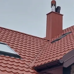 Czerwony dach z blachodachówki z oknem dachowym i kominem z nasadami wentylacyjnymi