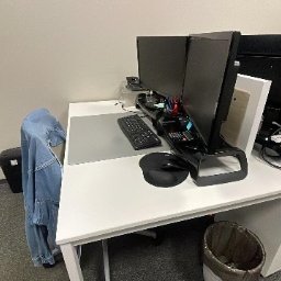 Cleaning Today Olga Belska - Białe biurko z dwoma monitorami, klawiaturą i myszką komputerową w biurze. Pod biurkiem widoczny kosz na śmieci. Na krześle wisi jeansowa kurtka.