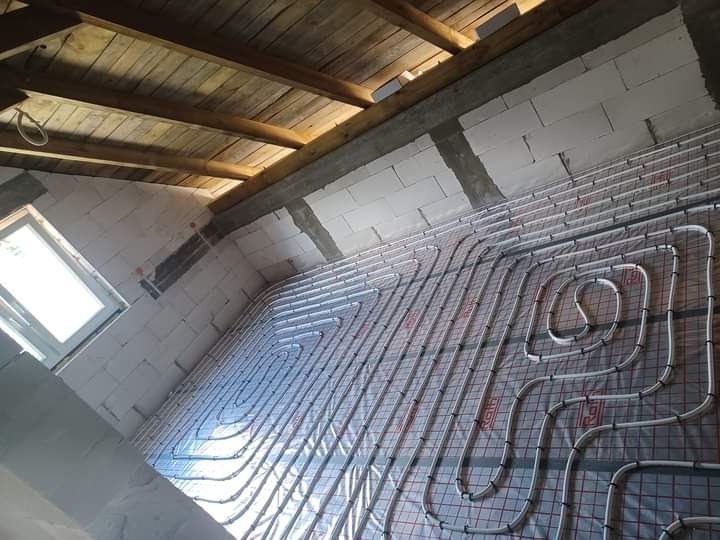 Montaż ogrzewania podłogowego w surowym wnętrzu poddasza z widoczną izolacją i drewnianą konstrukcją dachu.