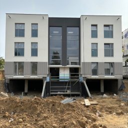 L.T.consulting - Dwukondygnacyjny budynek z szarą elewacją w trakcie prac wykończeniowych, widoczne rusztowania i ziemia przed budynkiem.