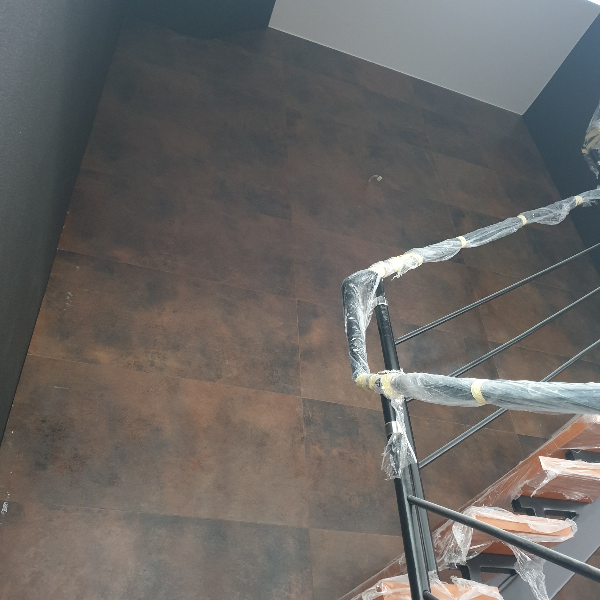 Ściana wyłożona brązowymi płytkami imitującymi kamień, zabezpieczone schody spiralne w folii ochronnej, widok z dołu