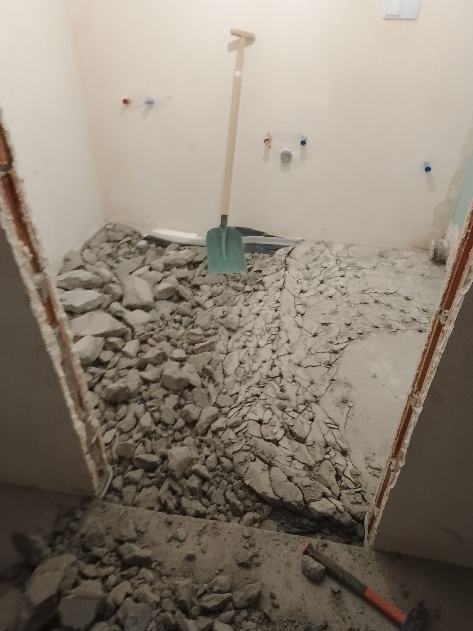 Demontaż posadzki w łazience, gruz na podłodze, widoczna łopata i młotek, przygotowanie do remontu.