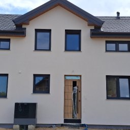 Jacek Hoeft - Dwukondygnacyjny dom z jasną elewacją i ciemnymi oknami. Widoczna pompa ciepła przy ścianie. Nowoczesny styl, świeżo po remoncie.