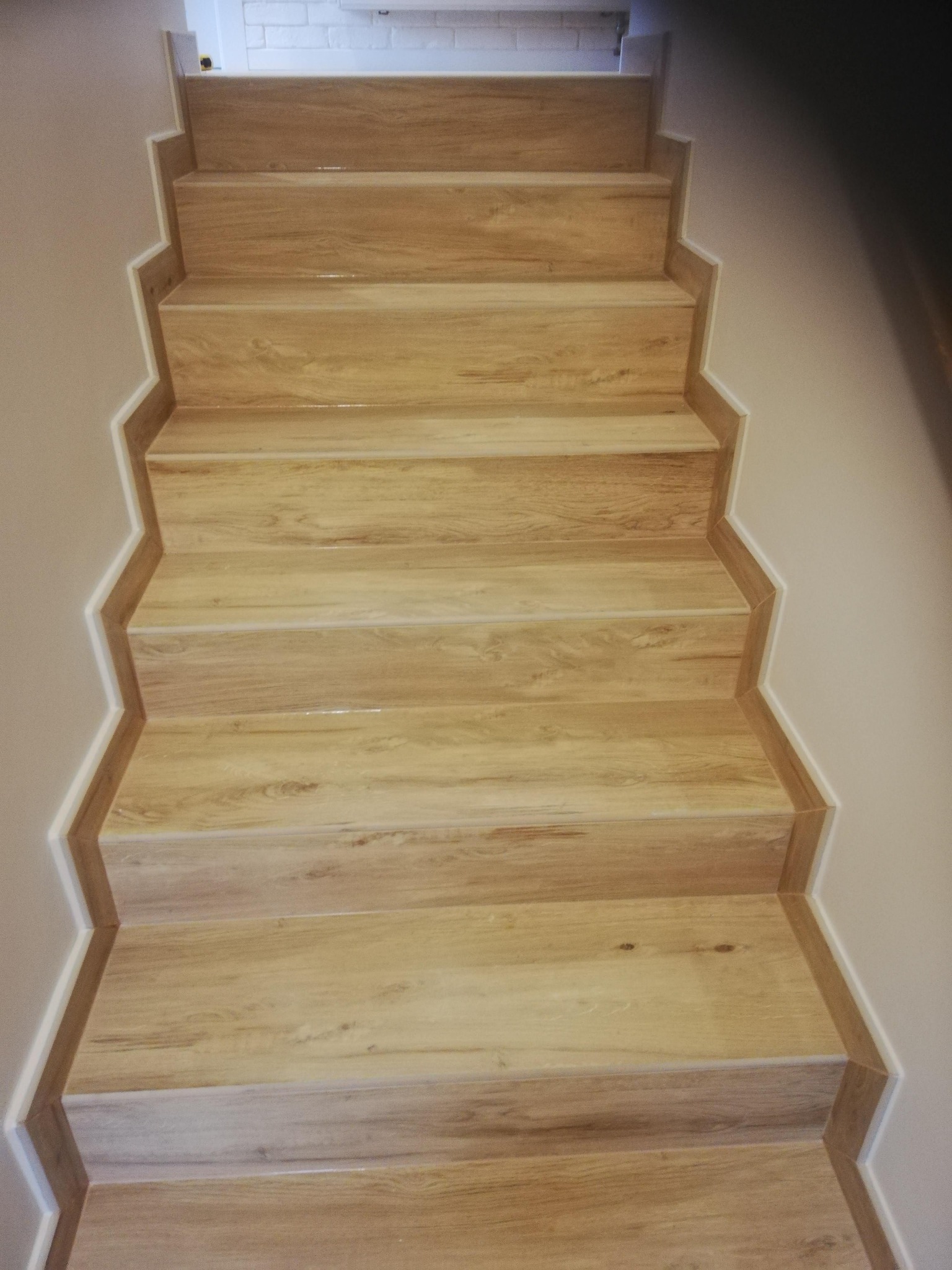 Wykończone schody z drewnopodobnych paneli, z białymi listwami przypodłogowymi. Widok z dołu, ukazujący detale wykończenia i strukturę materiału.