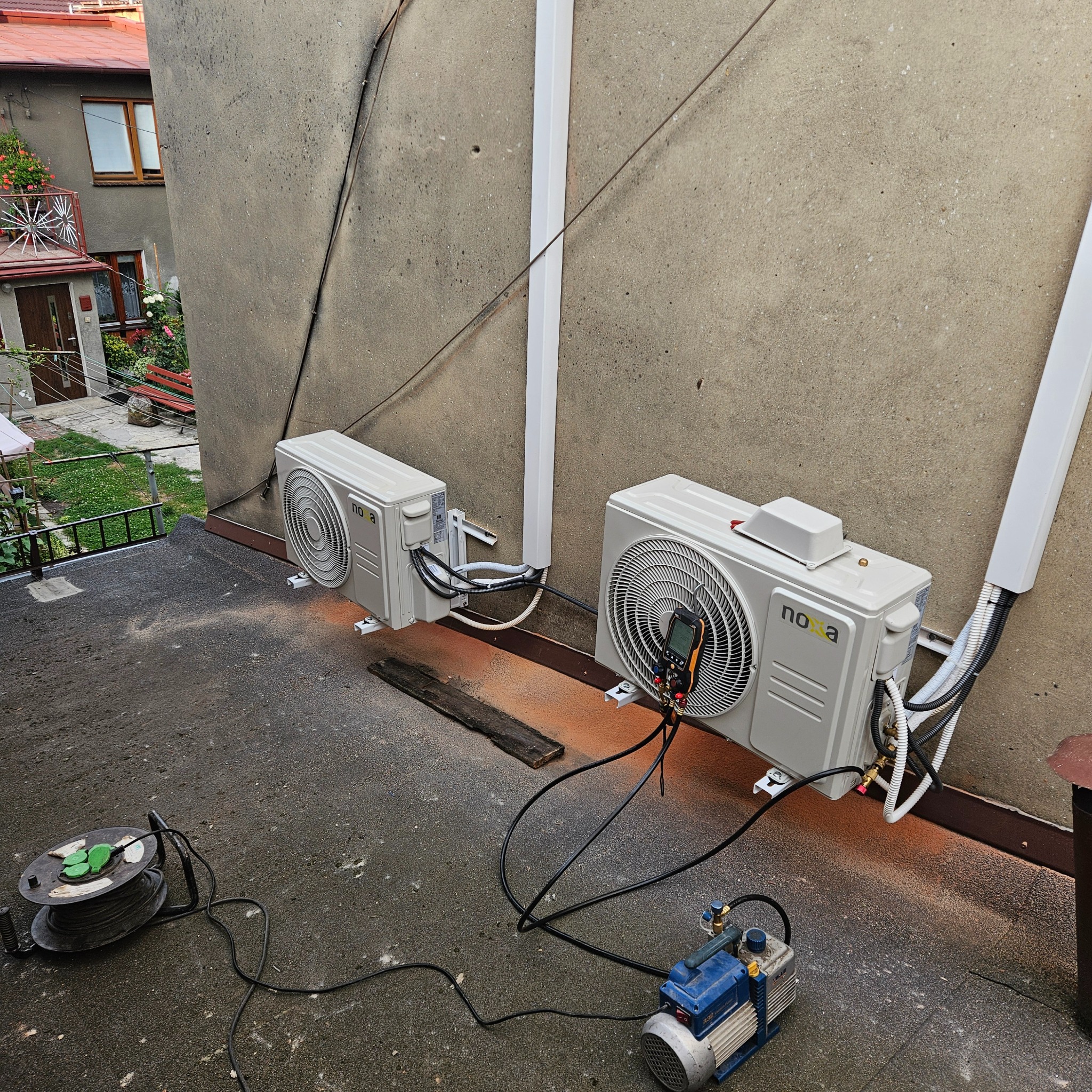 Dwa zamontowane klimatyzatory marki Nova na zewnątrz budynku, podłączone do pompy próżniowej i manometru podczas instalacji.