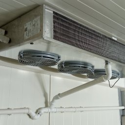 TT Inwest - Chłodnica przemysłowa z trzema wentylatorami zamontowana pod sufitem chłodni, widoczne białe rury instalacji chłodniczej.