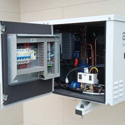 TT Inwest - Otwarta obudowa zewnętrznej jednostki chłodniczej z widocznymi elementami instalacji elektrycznej, automatyki i rurami chłodniczymi, z podłączonymi przewodami pomiarowymi.