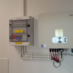TT Inwest - Rozdzielnica PV AC i falownik SOFAR Solar zamontowane na białej ścianie, połączone rurkami instalacyjnymi i kablami.
