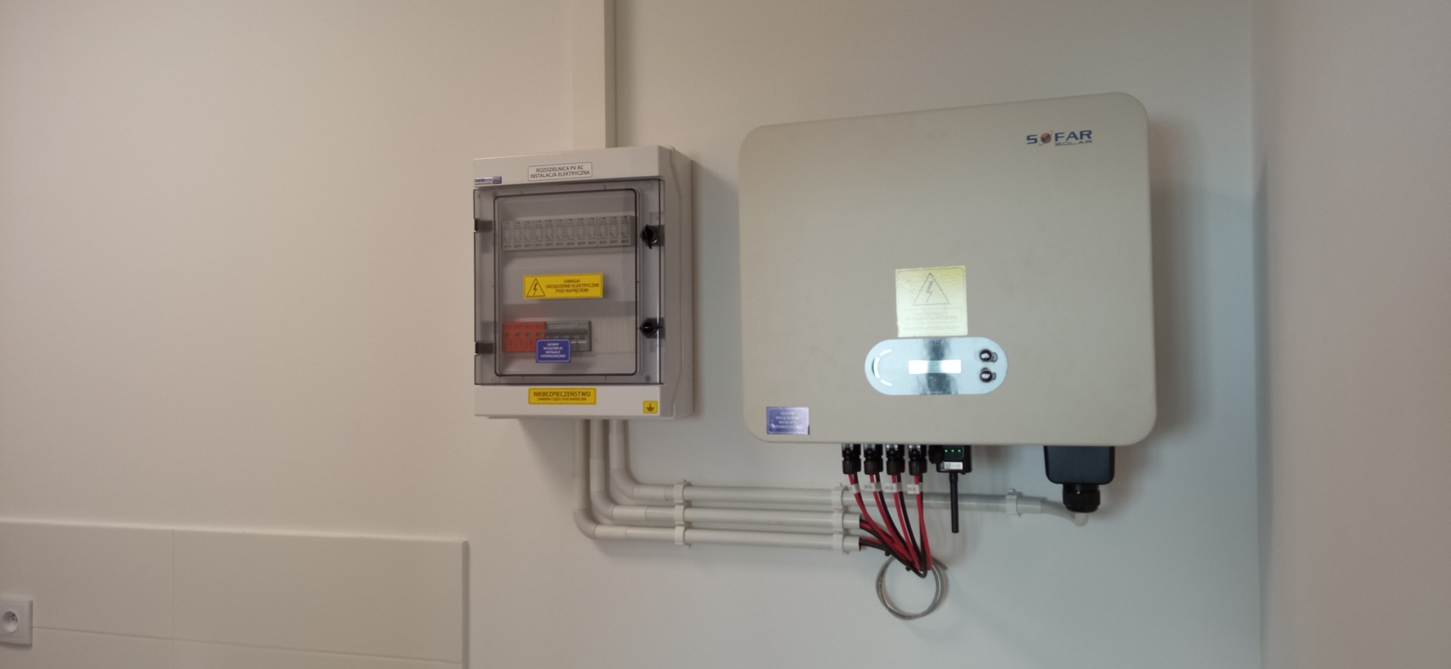 Rozdzielnica PV AC i falownik SOFAR Solar zamontowane na białej ścianie, połączone rurkami instalacyjnymi i kablami.