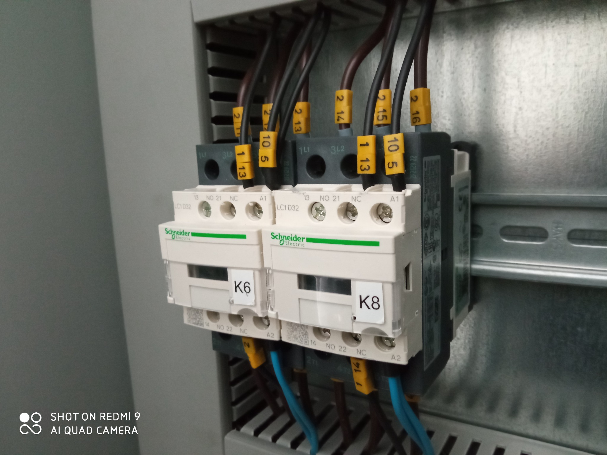 Dwa styczniki Schneider Electric LC1D32 z podłączonymi przewodami oznaczonymi numerami na żółtych etykietach, zamontowane w szafie sterowniczej, widoczne oznaczenia K6 i K8 na stycznikach.