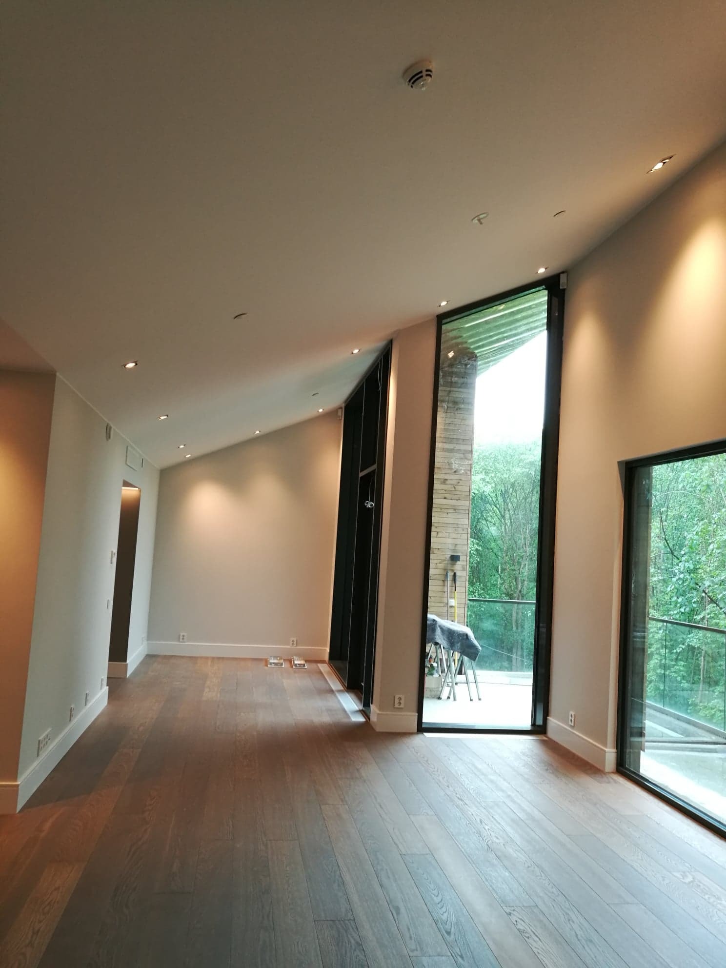 Jasne, przestronne wnętrze w Lubieniu po remoncie, z drewnianą podłogą, świeżo pomalowanymi ścianami i dużymi oknami z widokiem na zieleń. Widoczne listwy przypodłogowe i punkty oświetleniowe...