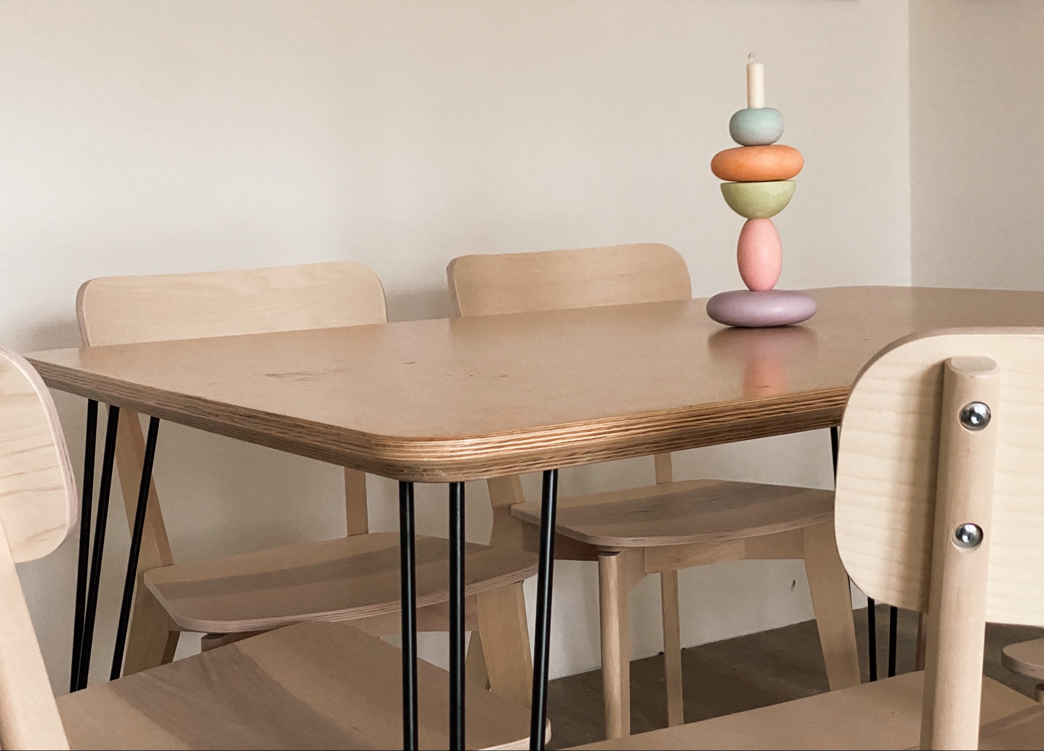 Stół z jasnego drewna z czarnymi metalowymi nogami i dopasowane krzesła, na blacie dekoracyjny świecznik z kolorowych drewnianych elementów.