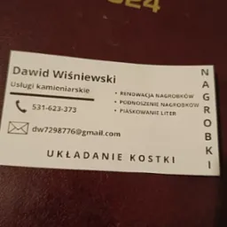 Wizytówka firmy kamieniarskiej Dawida Wiśniewskiego z numerem telefonu, adresem email, oferująca usługi renowacji, podnoszenia nagrobków, piaskowania liter oraz układania kostki, leżąca...