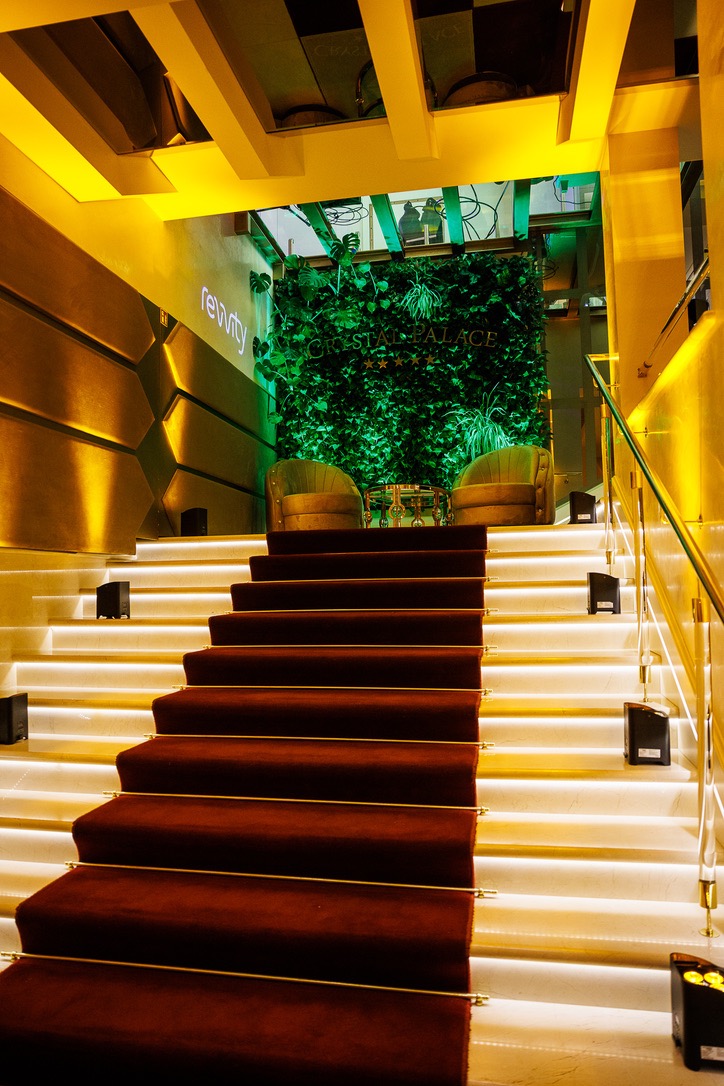 Schody z czerwonym dywanem prowadzące do zielonej ściany z napisem Crystal Palace, oświetlone punktowymi lampami i podświetleniem LED stopni.