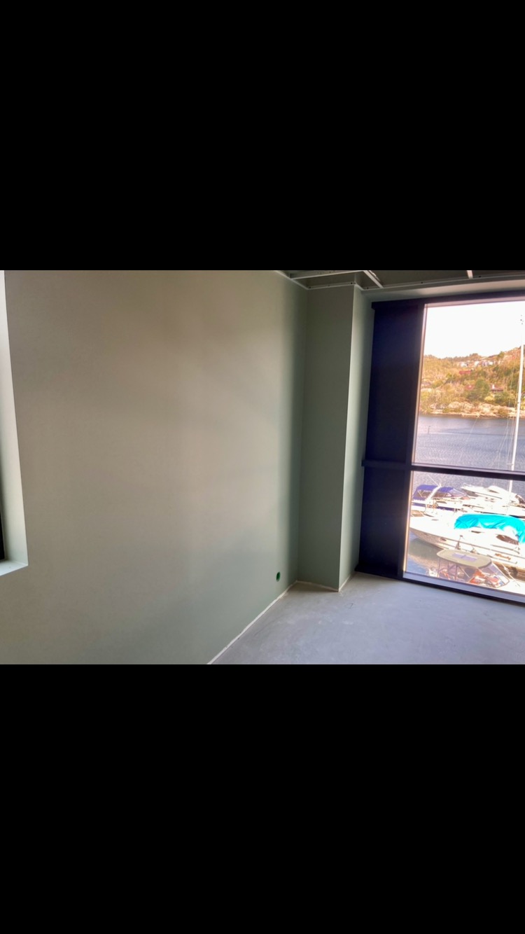 Świeżo pomalowane wnętrze w odcieniach zieleni z widokiem na przystań jachtową przez duże okno.