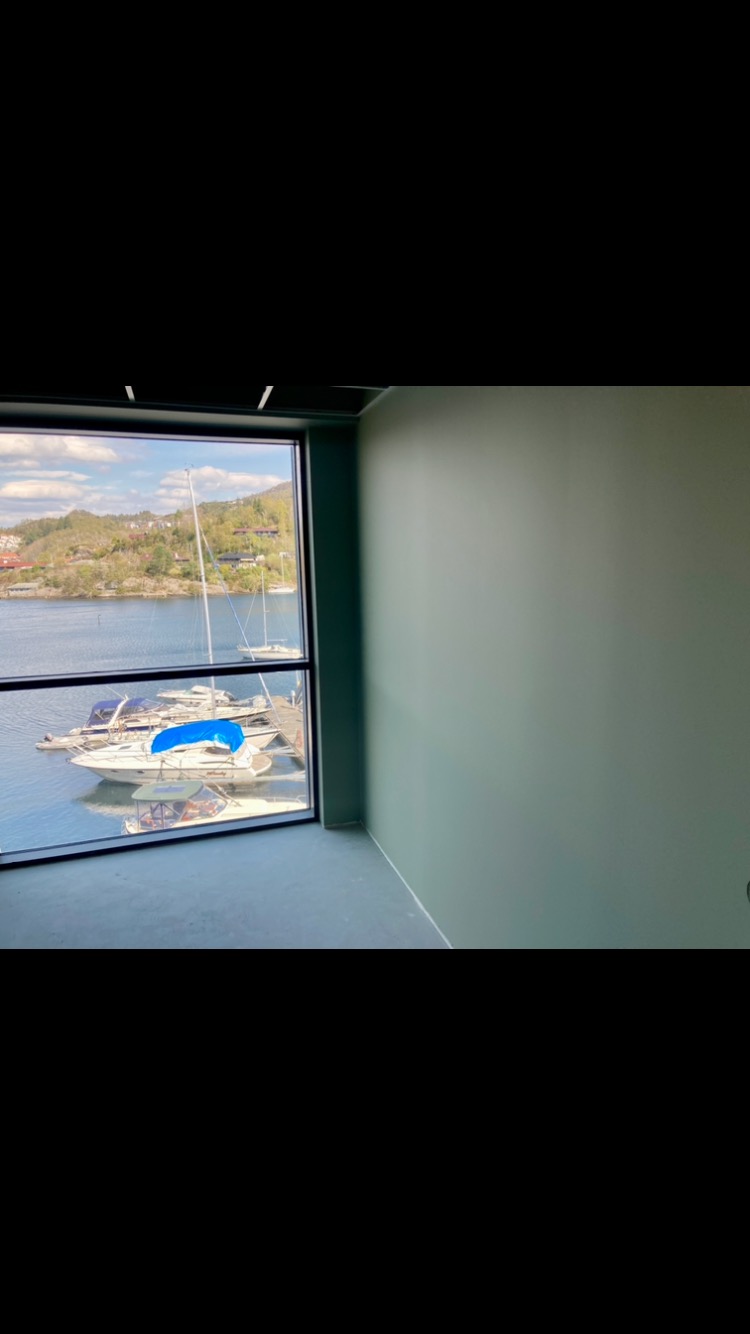 Pomalowane na pastelowo zielono wnętrze pokoju z widokiem na przystań jachtową przez duże okno.