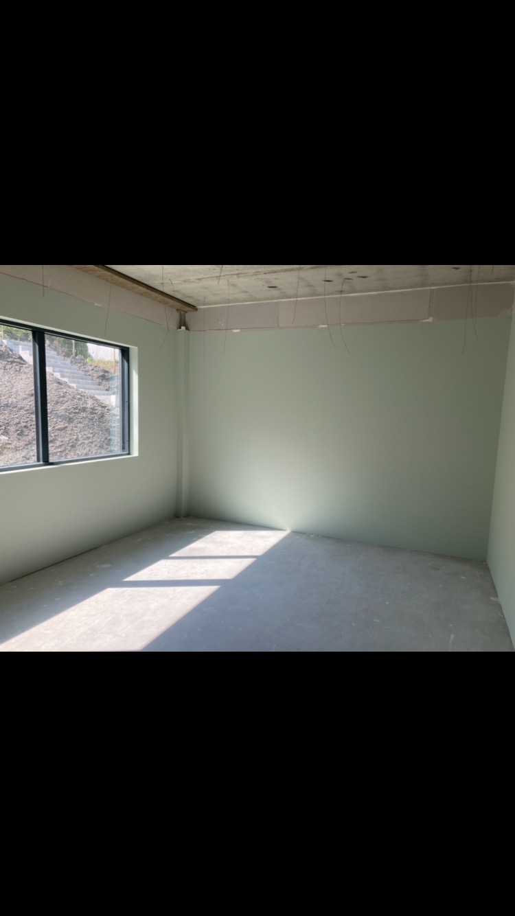 Wnętrze pokoju po szpachlowaniu i malowaniu na jasnozielono, z widocznymi przewodami zwisającymi z sufitu i światłem słonecznym wpadającym przez okno.