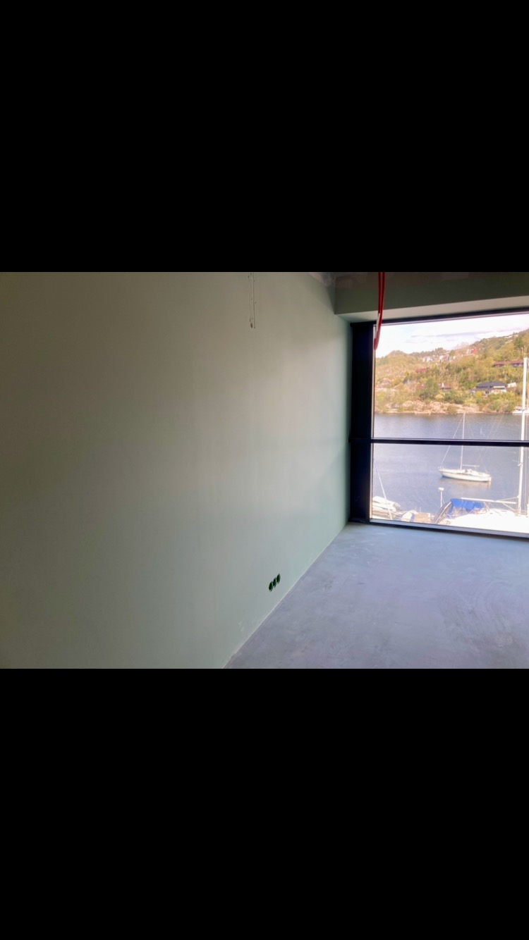 Jasnozielona ściana w nowym pomieszczeniu z widokiem na zatokę z jachtami przez duże okno.