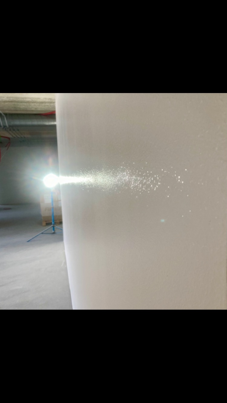 Światło lampy budowlanej oświetla świeżo wyszpachlowaną ścianę, ukazując jej strukturę i nierówności przed malowaniem.