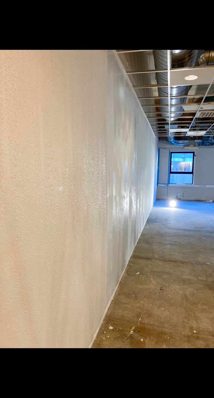 Ściana po nałożeniu gładzi, widoczne ślady po szpachlowaniu, surowy beton na podłodze, instalacja pod sufitem biura.