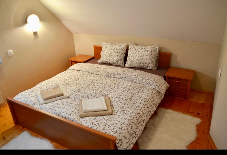 Pokój na poddaszu po odświeżeniu ścian: beżowe ściany, drewniane łóżko z pościelą w drobne kwiatki, drewniane szafki nocne i jasny dywanik.