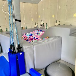 Gabinet Terapii i Rozwoju Dziecka Anna Dajnowska - Sala do terapii integracji sensorycznej: suchy basen z piłeczkami, podwieszane platformy, mata podłogowa z motywem gór i gwiazd, półkula do ćwiczeń równowagi.