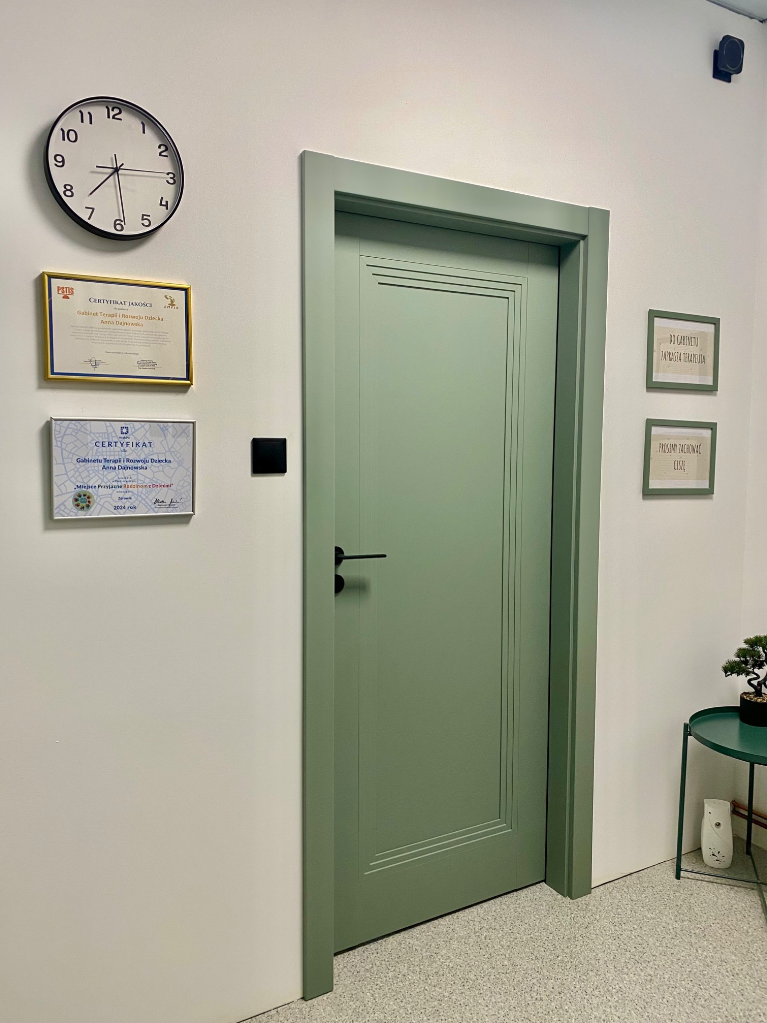Wnętrze gabinetu: zielone drzwi, zegar, certyfikaty (jakości i 'Miejsce Przyjazne Rodzinom z Dziećmi'), stolik z bonsai. Napisy: 'Do gabinetu zaprasza terapeuta', 'Prosimy zachować ciszę'.
