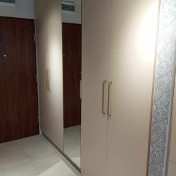 AGStolarstwo - Beżowa szafa na wymiar z lustrem w Krypnie Kościelnym, z długimi złotymi uchwytami i dekoracyjnym panelem bocznym z motywem roślinnym.