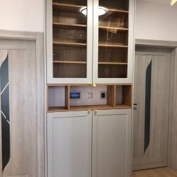 AGStolarstwo - Wysoka, szara szafa z przeszklonymi górnymi drzwiczkami i drewnianymi półkami wewnątrz, zintegrowana z panelem sterowania domem i oświetleniem LED, umieszczona między dwiema szarymi drzwiami.