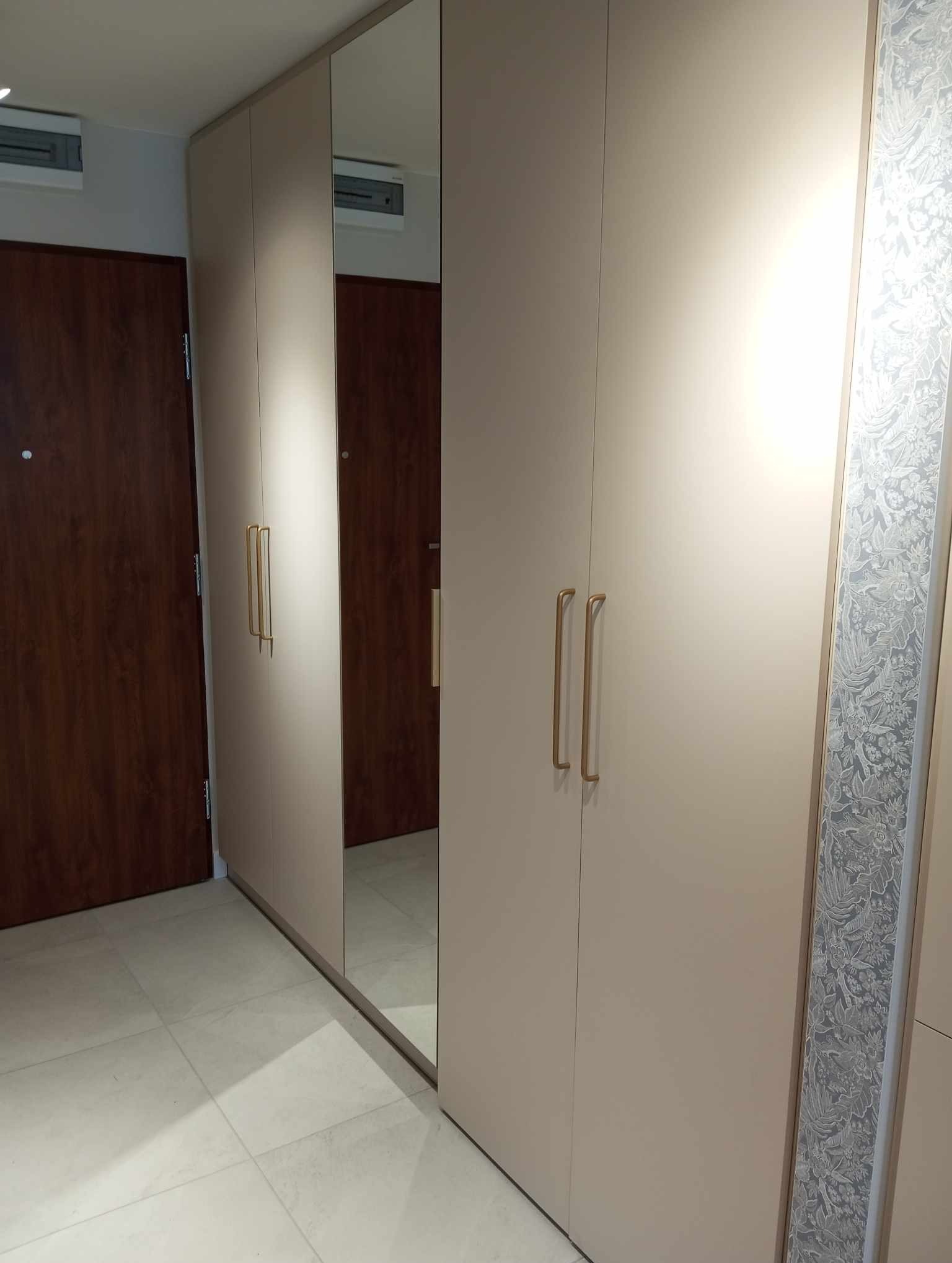 Beżowa szafa na wymiar z lustrem w Krypnie Kościelnym, z długimi złotymi uchwytami i dekoracyjnym panelem bocznym z motywem roślinnym.