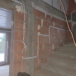 JG Instalacje Elektryczne - Wnętrze w stanie surowym: widoczne przewody elektryczne zamontowane na ścianach z cegły, betonowe schody i butelka Coca-Coli na jednym ze stopni.