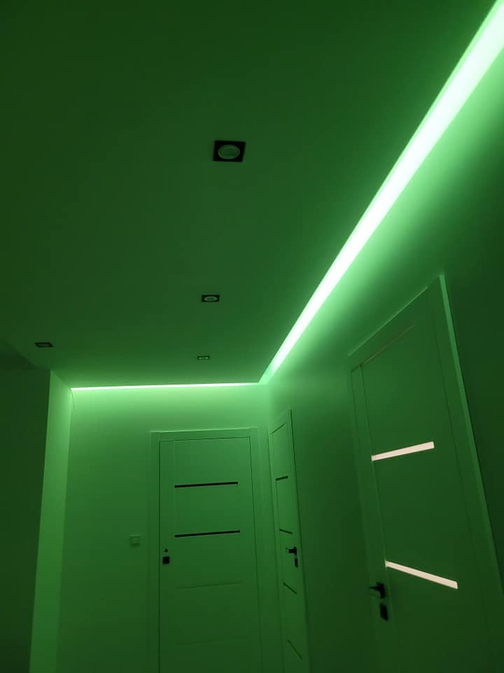 Korytarz oświetlony zielonym światłem LED, z widocznymi dwoma białymi drzwiami i punktowymi lampami sufitowymi.