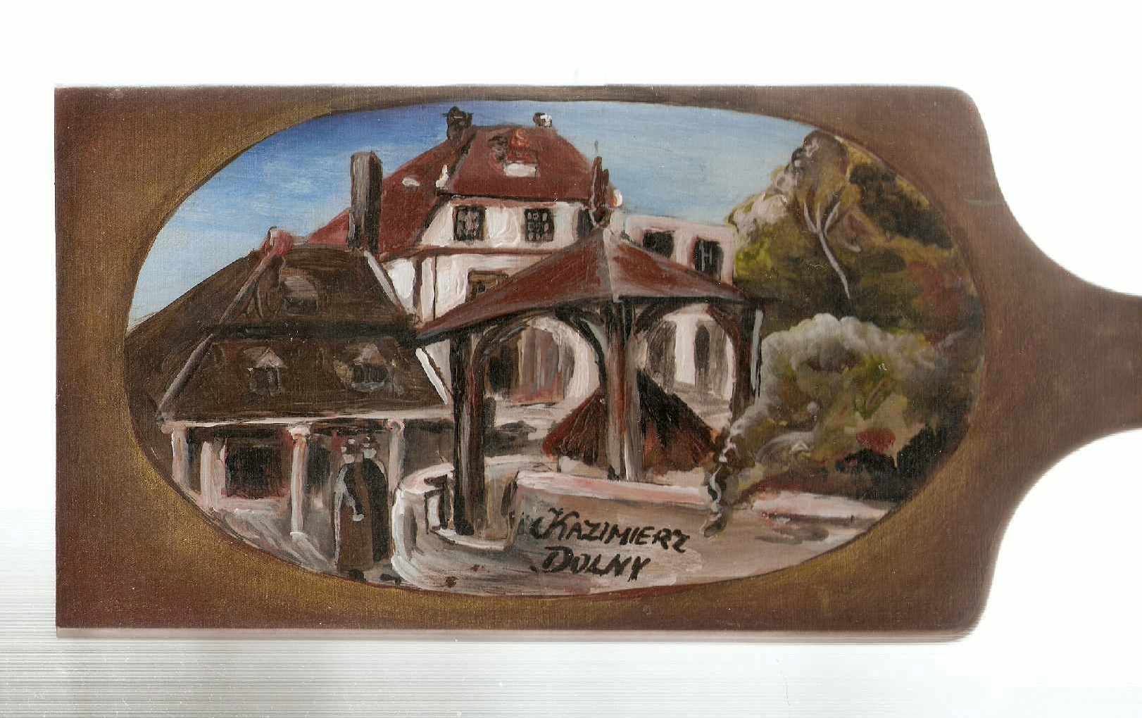 Ręcznie malowany obrazek na drewnianej desce przedstawiający zabudowania w Kazimierzu Dolnym, z charakterystyczną studnią i budynkami z czerwonymi dachami.