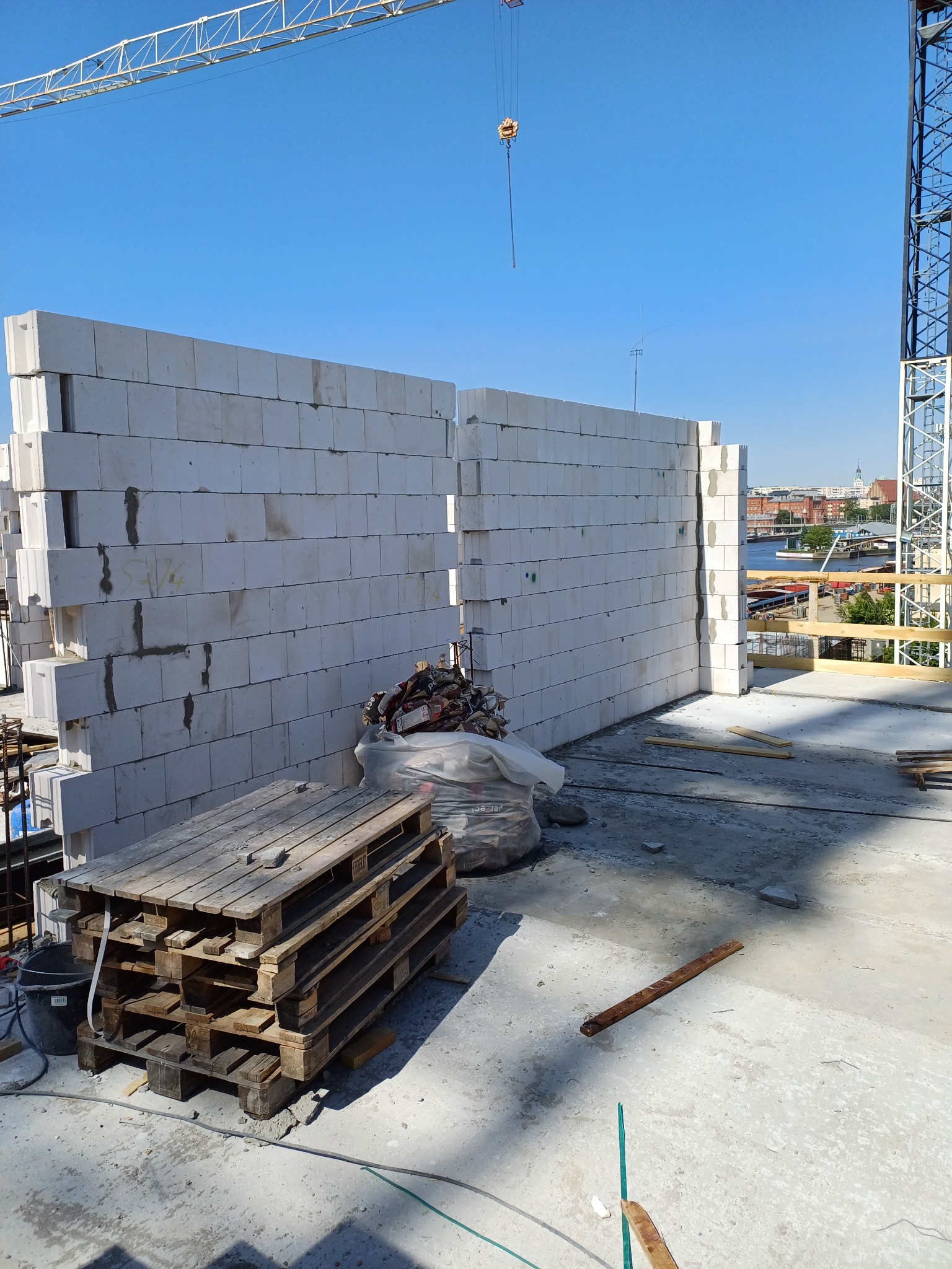 Wznoszenie ściany z białych bloczków betonu komórkowego na placu budowy, widoczny dźwig i paleta z materiałami.