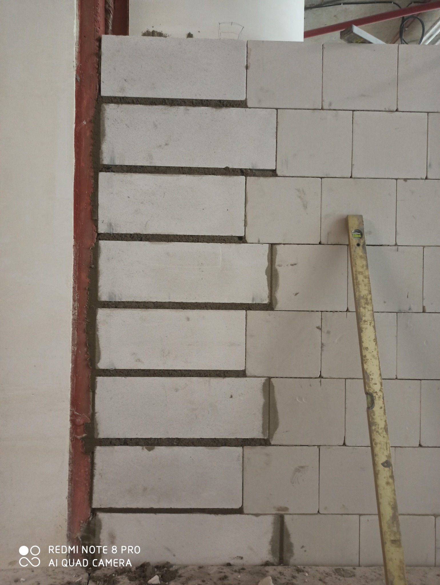 Ściana z betonu komórkowego w trakcie murowania w Szczecinie, widoczny poziomica i fragment metalowej konstrukcji.