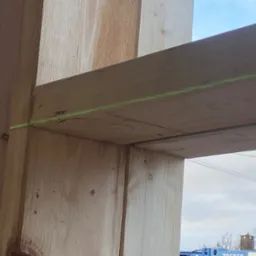 Fragment konstrukcji drewnianej w trakcie budowy, z widoczną poziomą linią lasera wyznaczającą poziom.