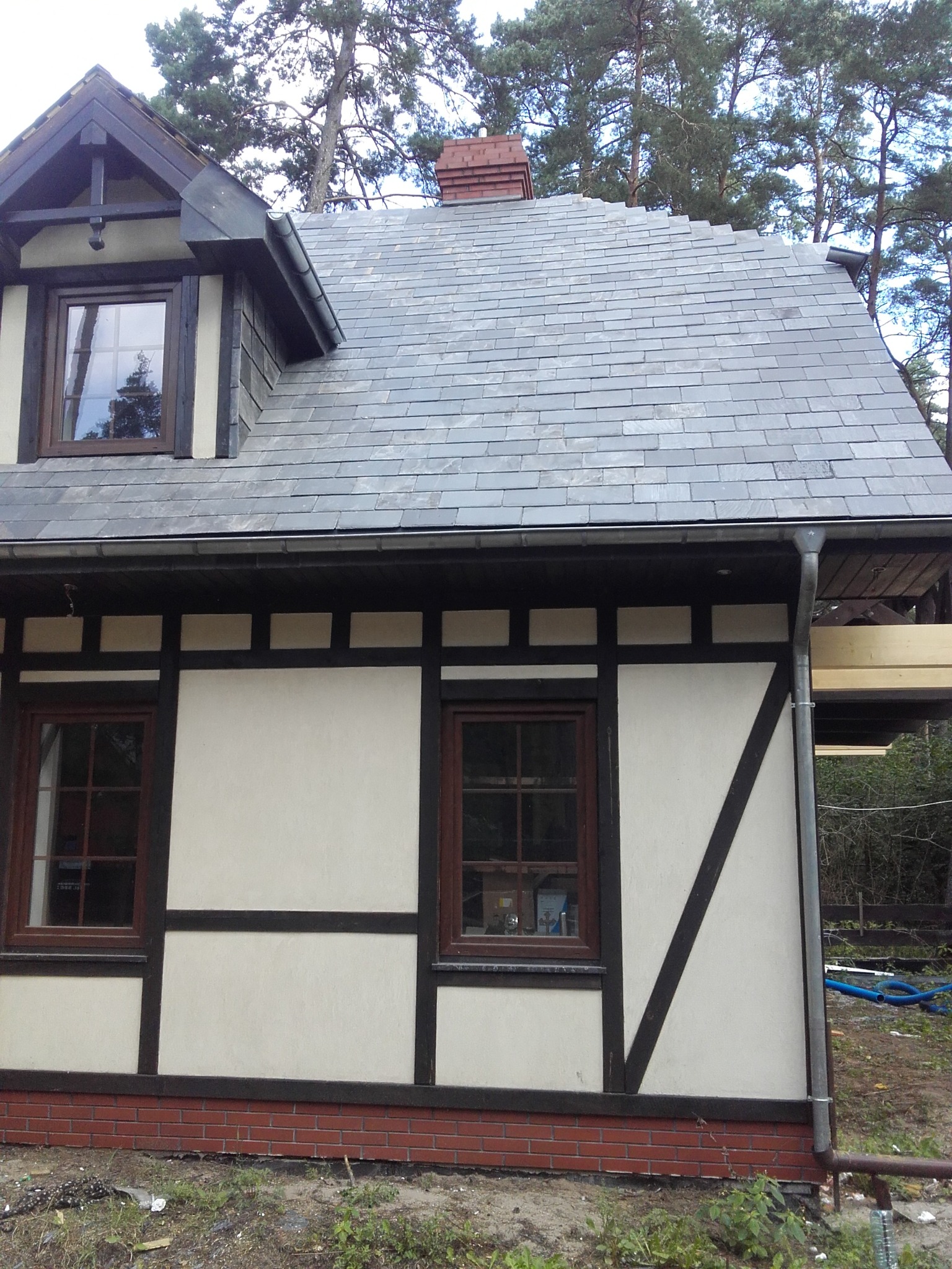 Fragment domu w stylu muru pruskiego z nowym dachem z szarej dachówki, widoczne elementy konstrukcyjne dachu i orynnowanie.