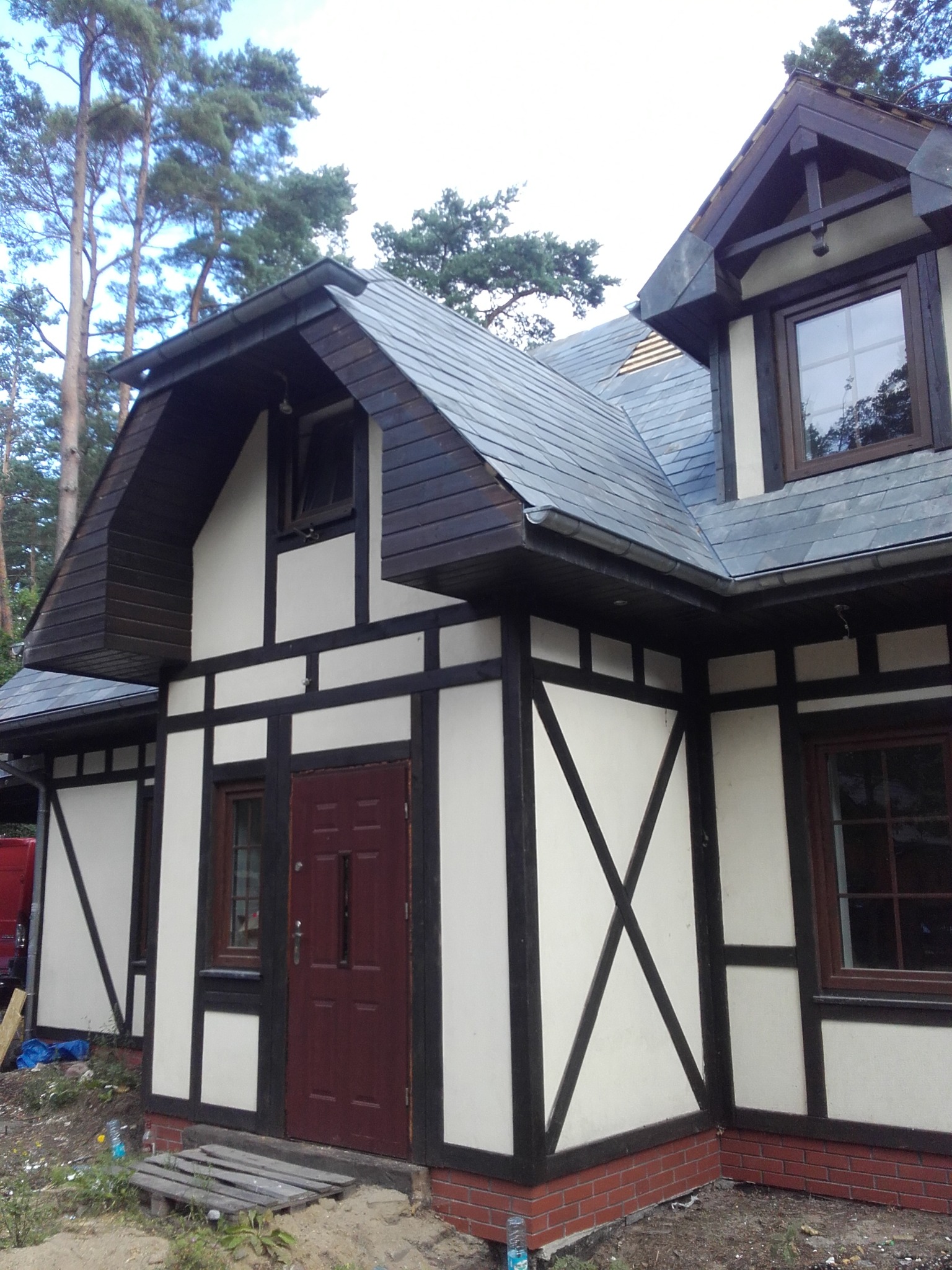 Nowo wybudowany dom w stylu szachulcowym z ciemną stolarką okienną i drzwiami, oraz dachem pokrytym szarą dachówką, widok z niskiej perspektywy.