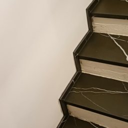 K. R. Firma remontowo - budowlana Radosław Kuchta - Schody wykończone czarnym marmurem z białymi żyłami, przylegające do białej ściany.