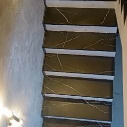 K. R. Firma remontowo - budowlana Radosław Kuchta - Schody wykończone czarnym marmurem z białymi żyłami, widok z góry na strukturę ściany i oświetlenie.