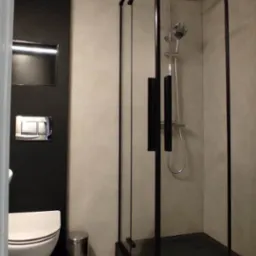 Nowoczesna łazienka z kabiną prysznicową typu walk-in z czarnymi profilami, wiszącą toaletą i okrągłym lustrem w suficie.