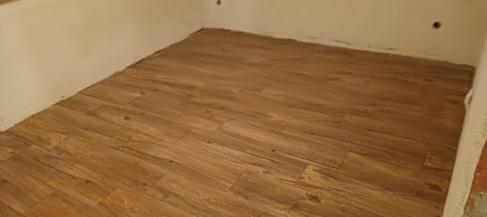 Ułożone panele podłogowe w rogu pomieszczenia, widoczne niedoskonałości wykończenia przy ścianach.