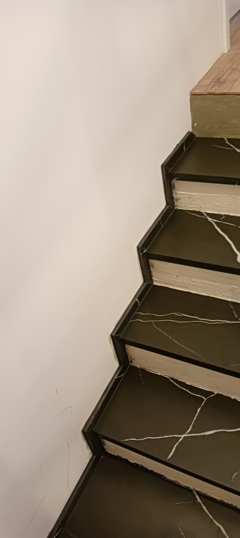 Schody wykończone czarnym marmurem z białymi żyłami, przylegające do białej ściany.